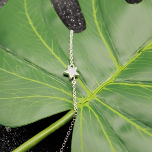 Detail of silver star charm bracelet on a green leaf with black textured background