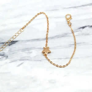 Macro view of adjustable gold star pendant bracelet with lobster clasp on marble
