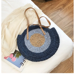 Détail du sac cabas rond en paille avec rayures bleues et poignées en similicuir marron