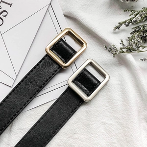 Detail of black PU leather belts with gold and silver square buckles on white fabric