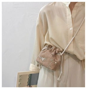 Detail of straw bucket bag with floral embroidery and white cotton rope strap