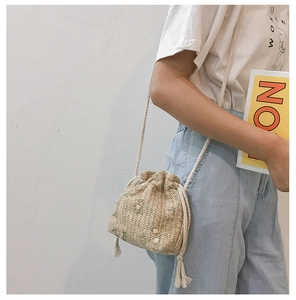 Detail of a straw bucket bag with floral embroidery and white drawstring strap