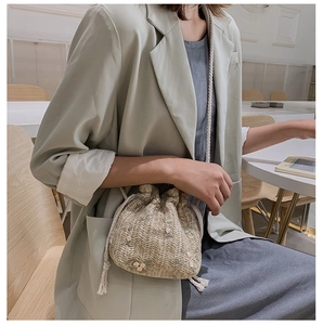 Detail of woven straw bucket bag featuring delicate floral embroidery and drawstring closure