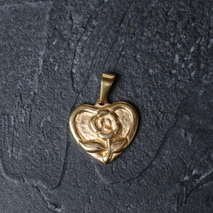 Close-up of golden heart pendant featuring a 3D embossed rose on textured stone