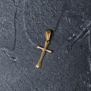 Close-up of a minimalist gold-plated stainless steel cross pendant on a textured dark background