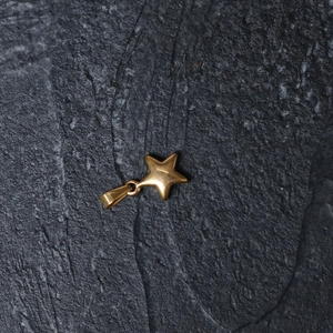 Close-up of a polished gold star pendant made of stainless steel on a dark slate background