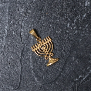 Close-up of gold-plated stainless steel Menorah pendant on a grey textured stone surface