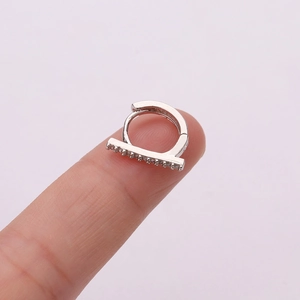 Close-up of a silver cartilage earring with micro-paved zircons held on a finger