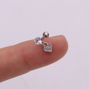 Detail of silver heart charm helix earring with zircon stone held on fingertip for size