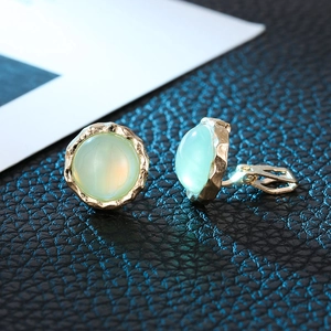 Detail of gold clip-on earrings with light green opal stone on black leather surface