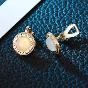 Detail of gold-framed clip-on earrings with white opal resin stones on blue leather