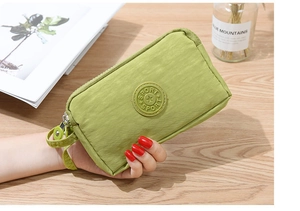 Dettaglio di pochette in tessuto verde chiaro con tre cerniere e cinturino da polso