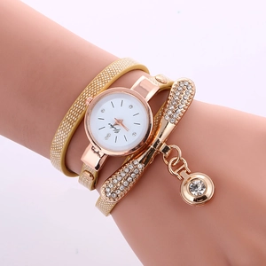 Close-up of golden wrap-around watch with rhinestone bow and sparkling pendant on wrist