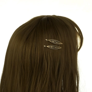 Détail de deux pinces à cheveux dorées en forme de feuille sur cheveux bruns