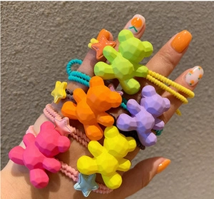 Close-up of colorful resin bear hair ties in green, orange, purple, and pink on a wrist