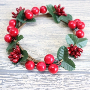 Detailed close-up of Christmas candle ring with red berries, green leaves and rattan base