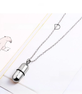 Macro view of screw-open stainless steel capsule pendant with fine cross chain on a book