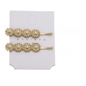 Detail of 5.7cm golden daisy hair clips with white pearls on a display card