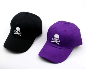 Close-up of skull and crossbones embroidery on black and purple cotton baseball caps