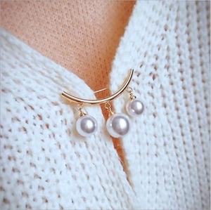 Detailed view of a gold brooch with three white pearl pendants on white knit sweater