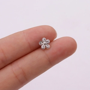Close-up of small silver flower stud earring with clear zircon petals held in fingers