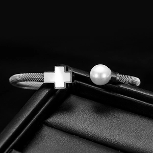 Makro-Detail von silbernem Kabelarmband mit Perle und Kreuz-Inlay auf schwarzem Leder
