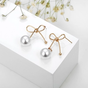 Elegante goldene Schleifenohrringe mit weißen Perlen auf weißem Sockel mit Trockenblumen