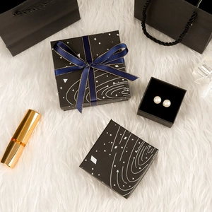 Black starry jewelry gift boxes with blue ribbon and matching paper bag on white plush surface