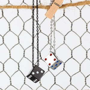 Minimalist luck dice pendant necklaces in silver and black hanging on a wire fence