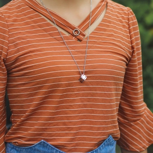 Minimalist silver dice pendant necklace for couples shown worn by a model in nature