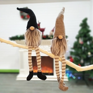 Close-up of two long-legged Christmas gnomes on a wooden branch with festive background