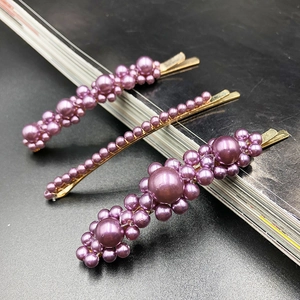 Close-up of three purple pearl hair clips with gold alloy base on dark background