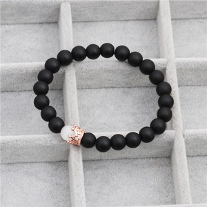 Detail of matte black beads bracelet with a rose gold crown charm on grey jewelry tray