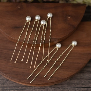 Close-up of golden U-shaped hair pins with white pearls on a dark wooden background
