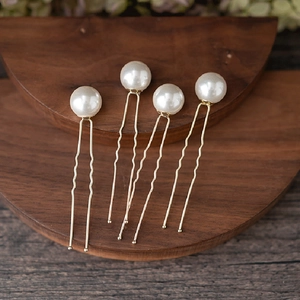 Macro view of four elegant white pearl U-shaped hair pins on a dark wood stand