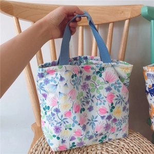 Florale Baumwolltasche mit blauen Henkeln auf einem rustikalen Holzstuhl platziert