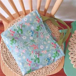 Detail einer hellblauen Stofftasche mit Blumenmuster und grünen Tragegriffen auf Stuhl
