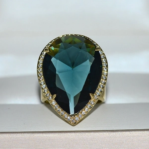 Macro shot of luxury gold-tone ring featuring a pear-cut teal gemstone with pavé diamonds