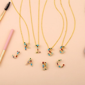 Flat lay of colorful zircon alphabet necklaces spelling KISS on pink background