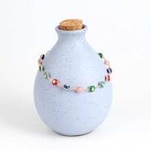 Detail of colorful evil eye beads on a gold chain draped over a ceramic bottle neck