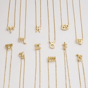 Flat lay of 12 gold plated stainless steel necklaces featuring zodiac symbol pendants