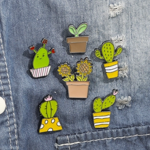 Detail of five enamel cactus and sunflower plant brooches on a blue denim jacket