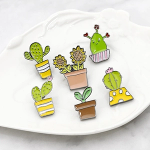 Detailed view of six enamel cactus and sunflower pins in a white leaf-shaped ceramic dish