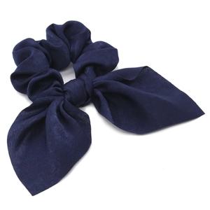 Detailed view of navy blue satin scrunchie with long ribbon bow on white background