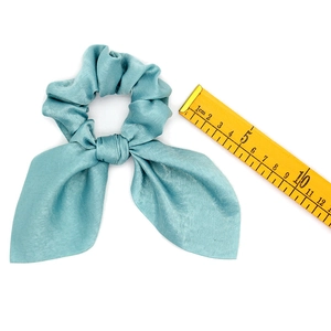 Detailed view of a light blue satin scrunchie with bunny ears next to a scale ruler