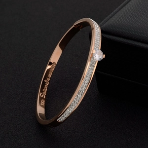 Rose gold bangle with double rows of crystals and a center diamond on black background
