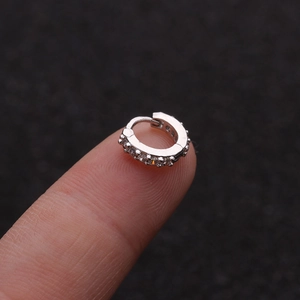 Macro shot of a mini silver zircon hoop earring resting on a fingertip showing fine details