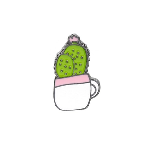 Macro detail of cartoon cactus enamel pin in a white mug with polished metal finish