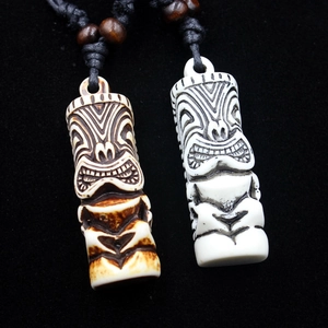 Detailed view of two faux bone Tiki pendants with tribal mask carvings on black cord