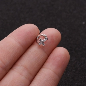 Close-up of silver micro-pave cubic zirconia cross cartilage earring held by fingers